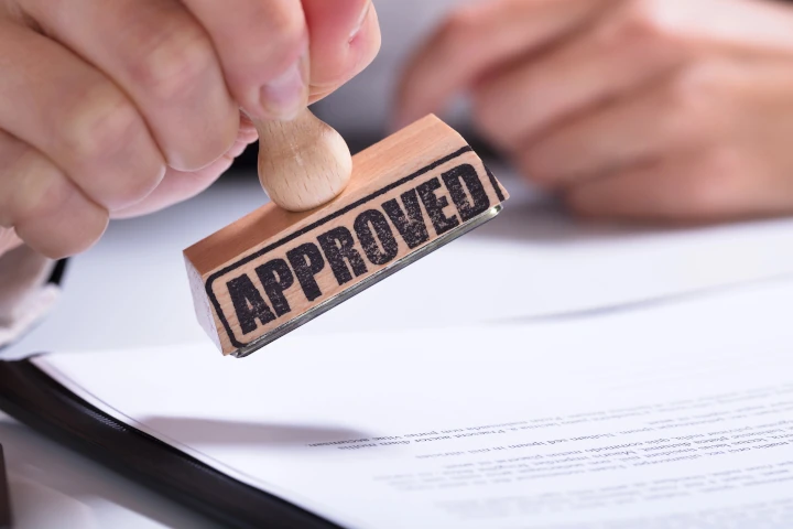Hands Applying Approved Stamp On Document