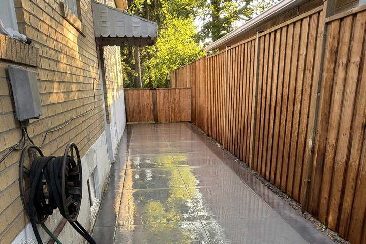 Clean cedar fence maintenance line running along a wet stone walkway during fall prep in the GTA.